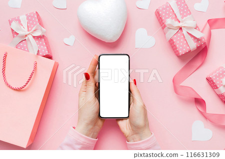 Woman hand holding mobile phone with blank screen on colored background with hearts, valentine day concept top view flat lay 116631309