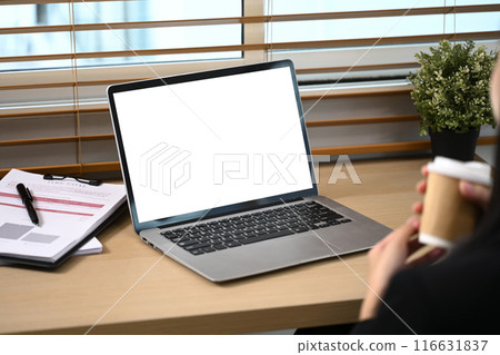Laptop with blank screen and financial document on wooden table in front of businesswoman Laptop with blank screen and financial document on wooden table in front of businesswoman 116631837