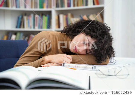 Tired female architect working in library with blueprints and falling asleep Tired female architect working in library with blueprints and falling asleep 116632429