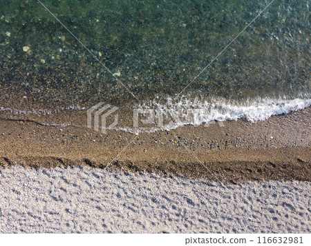 Aerial view from above on calm azure sea and pebbles beach. Small waves on cristal clear water surface in motion blur. Summer ocean sea beach background. Nobody. Holiday, vacation and travel concept Aerial view from above on calm azure sea and pebbles beach. Small waves on cristal clear water surface in motion blur. Summer ocean sea beach background. Nobody. Holiday, vacation and travel concept 116632981