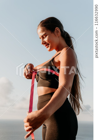 A woman is holding a pink tape measure and is measuring her chest after morning fitness A woman is holding a pink tape measure and is measuring her chest after morning fitness 116632990
