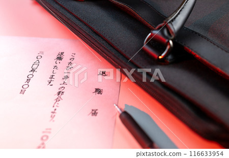 紅色燈光顯示白色桌子上的一封手寫辭職信、黑色中性墨水筆和黑色商務包的一部分。 紅色燈光顯示白色桌子上的一封手寫辭職信、黑色中性墨水筆和黑色商務包的一部分。 116633954