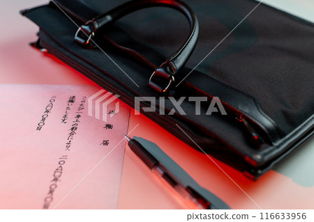 Handwritten resignation letter placed on a white table with a black gel ink pen and a black business bag with red lighting. 116633956