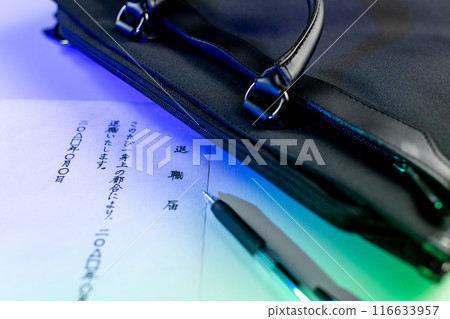 A handwritten resignation letter, a black gel ink pen, and part of a black business bag placed on a white table, illuminated with blue lighting. 116633957