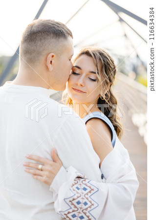 A Loving Couple Is Seen Embracing Each Other on a Beautiful Bridge on a Sunny Day, Surrounded by the Warmth of the Sun A Loving Couple Is Seen Embracing Each Other on a Beautiful Bridge on a Sunny Day, Surrounded by the Warmth of the Sun 116634384