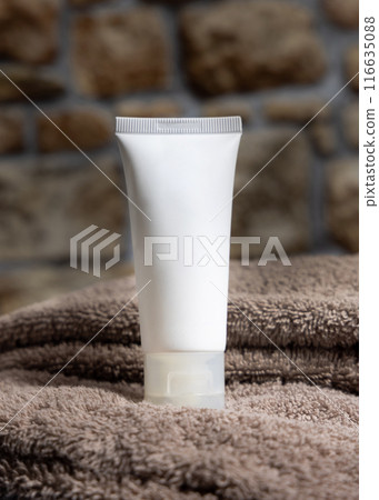 White cream squeeze tube on brown folded towel against stone wall close up, cosmetic mockup 116635088