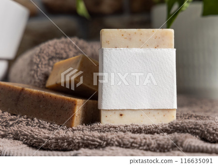 Soap bar with blank label on brown towel near sink and plant in bathroom closeup, mockup 116635091