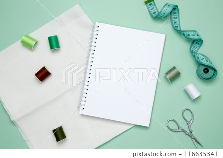 Composition with various threads and sewing accessories on green background. Mock up notebook 116635341