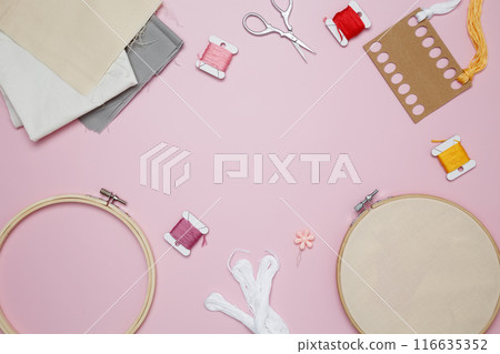Embroidery set fot stitching. Beige cotton cloth in embroidery hoop on pink background with fabric, colorful threads, scissors and needls 116635352