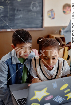 Vertical shot of two interested kids looking at laptop screen engaged in lesson with integrated educational technology, copy space 116636880