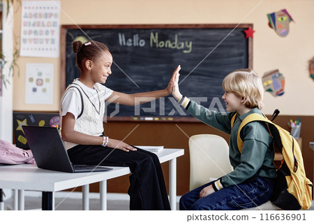 Side view shot of multiethnic classmates having fun together giving high five during break at school 116636901