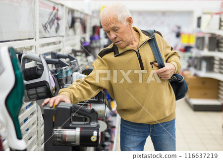 Senor man pensioner buying Upright Vacuum Cleaner in showroom of electrical appliance store 116637219