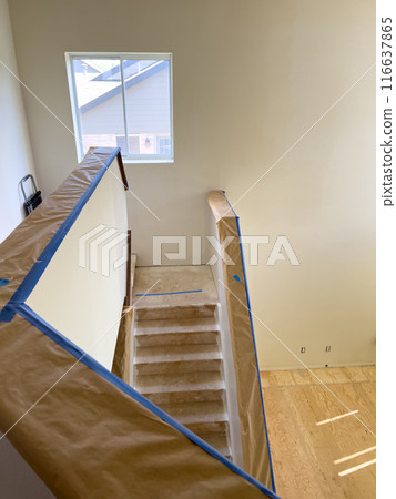 A well-lit stairway prepared for renovation, with protective paper and tape covering the banister. The steps are bare, indicating a work-in-progress state. The window in the background allows natural 116637865