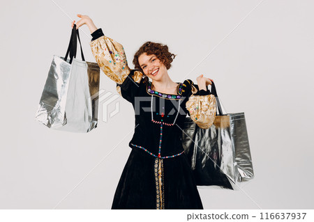 Young adult woman dressed in a medieval dress holding shopping bags in hands isolated white background 116637937