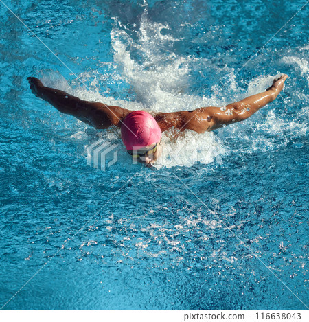 Athlete in pink swim cap and goggles executes butterfly stroke in pool, capturing intensity and movement of competitive swimming in action. 116638043