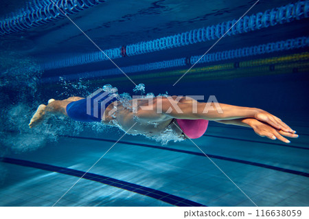 Dedicated swimmer in streamlined position, wearing pink cap and blue trunks, showcasing his toned physique and competitive focus. 116638059