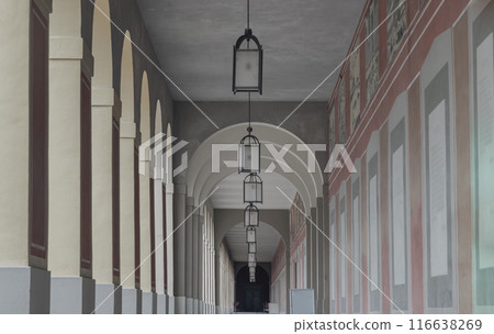 Long corridor with Antique lantern hanging from ceiling and Beautiful columns inside Hofgartenarkaden. Long corridor with Antique lantern hanging from ceiling and Beautiful columns inside Hofgartenarkaden. 116638269