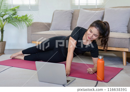 Young Woman Exercising at Home with Laptop, Performing Side Plank on Yoga Mat in Living Room 116638391
