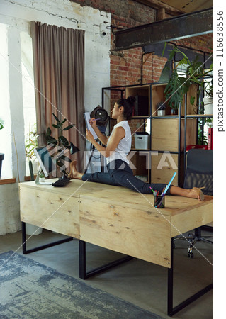 Woman, office worker sitting on twine on her working desk, making notes on documents. Physical wellness and productivity. 116638556