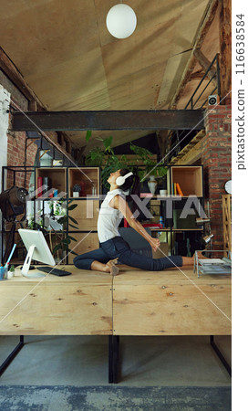 Woman, employee sitting on desk in headphones and practicing yoga and stretching exercises. Physical well-being Woman, employee sitting on desk in headphones and practicing yoga and stretching exercises. Physical well-being 116638584