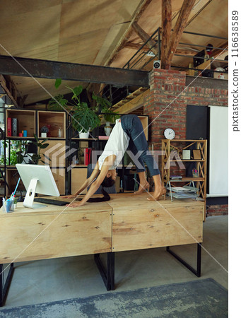 Woman in formal attire standing on desk around computer and office supplies and doing stretching exercises. Blending of work and health Woman in formal attire standing on desk around computer and office supplies and doing stretching exercises. Blending of work and health 116638589