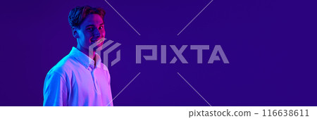 Portrait of young smiling guy, in white polo shirt, expressing confidence against gradient blue purple background in neon light. 116638611