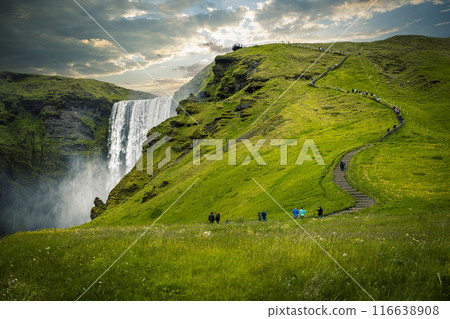 Tourists walking up path with waterfall and green grass in iceland 116638908