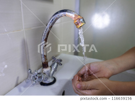 A child washes his hands with water from a rusty tap. Old plumbing, damage and fungus, rust. Unsanitary conditions in the bathroom 116639156