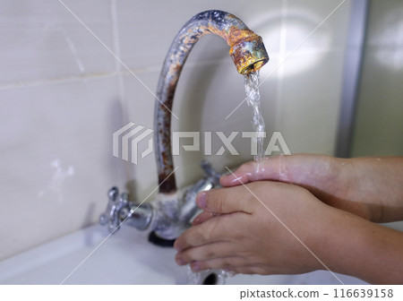 A child washes his hands with water from a rusty tap. Old plumbing, damage and fungus, rust. Unsanitary conditions in the bathroom 116639158