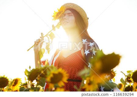Beautiful girl in hat with the American flag in a sunflower field. 4th of July. Fourth of July. Freedom 116639294