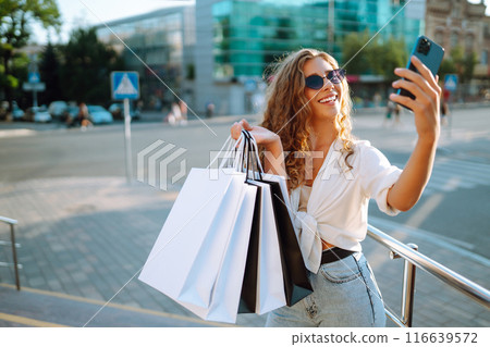 Beautiful woman with shopping bags makes selfie. Young woman walking shopping. Lifestyle concept. 116639572