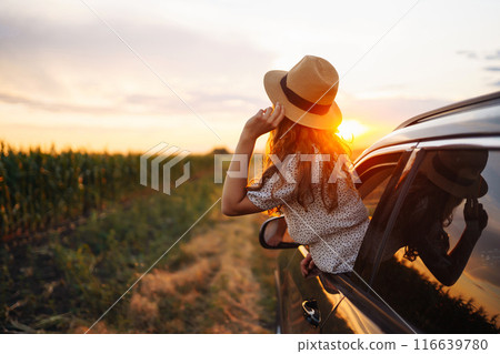Young happy woman in hat enjoys car ride, leaning out of window. Active lifestyle, travel concept. 116639780