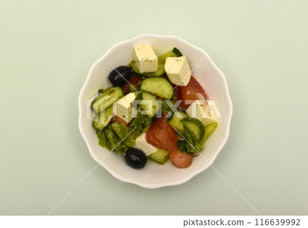 Greek salad in a white cup on a green background. Greek salad in a white cup on a green background. 116639992