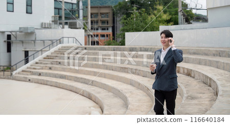 Young Professional Businessman Talking on Phone and Holding Coffee Cup in Outdoor Amphitheater 116640184