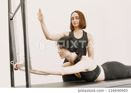 Young fit woman with a female trainer in gym. Woman wearing black sportwear. Caucasian girl lying on her belly. Young fit woman with a female trainer in gym. Woman wearing black sportwear. Caucasian girl lying on her belly. 116640405
