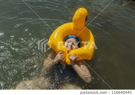 A portrait of a nine-year-old girl with a funny face inside a yellow inflatable duck float. She is smiling and enjoying her summer vacation while floating in the lake A portrait of a nine-year-old girl with a funny face inside a yellow inflatable duck float. She is smiling and enjoying her summer vacation while floating in the lake 116640445
