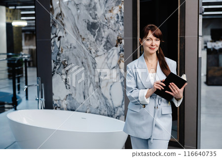 Woman in blue suit standing near freestanding tub in bathroom showroom 116640735