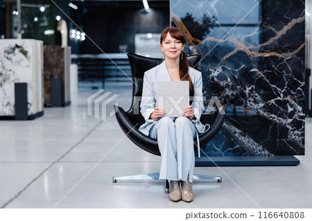 Woman holding blank paper sitting in chair in showroom 116640808