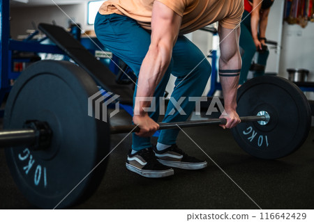 A bodybuilder showcases strength and athleticism by lifting weights in the gym 116642429