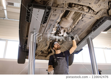 Mechanic inspecting car undercarriage at auto repair shop Mechanic inspecting car undercarriage at auto repair shop 116642476