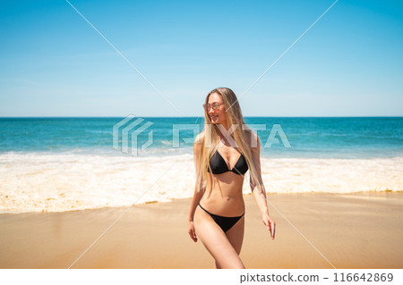 Happy blond woman in bikini walking near sea at 116642869