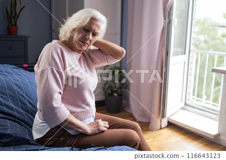 senior woman suffering from neck pain sitting at home alone 116643123