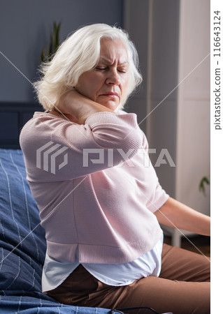 senior woman suffering from neck pain sitting at home alone 116643124