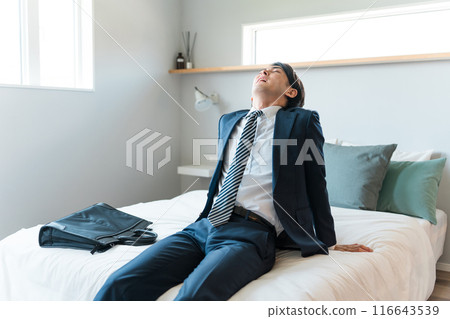 A young businessman in a tired suit sitting on the bed (drinking too much, hungover, returning home in the morning, drunk) A young businessman in a tired suit sitting on the bed (drinking too much, hungover, returning home in the morning, drunk) 116643539