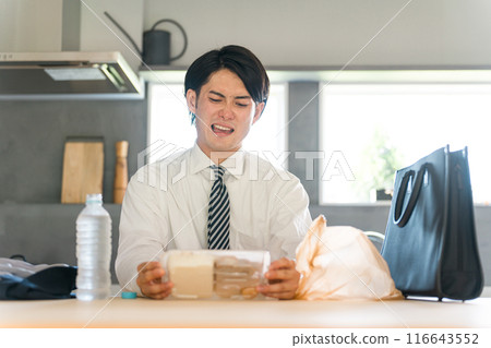 Asian businessman in a suit opening a convenience store bento in the dining room after returning home 116643552