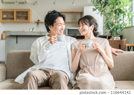 A friendly young Japanese couple relaxing on the sofa in their living room 116644142