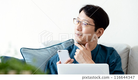 A middle-aged man operating a computer and smartphone on the sofa A middle-aged man operating a computer and smartphone on the sofa 116644347