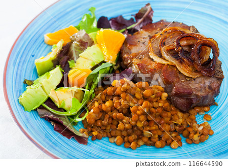 Delicious fried pork with lentils, avocado and orange at plate 116644590