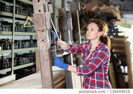 Adult woman processes metal part in workshop 116644658