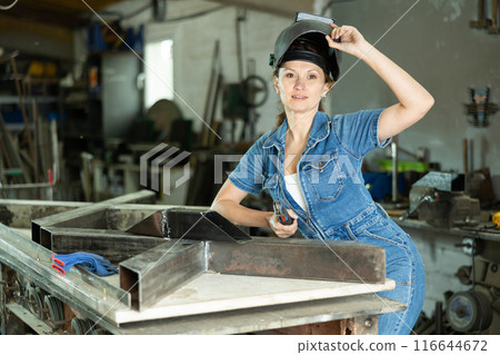 Portrait of a female welder standing with a welding semi-automatic machine and a safety helmet in metal machining workshop Portrait of a female welder standing with a welding semi-automatic machine and a safety helmet in metal machining workshop 116644672